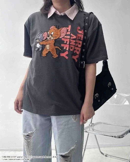 Person wearing a grey T-shirt with Tom and Jerry characters, styled with distressed jeans