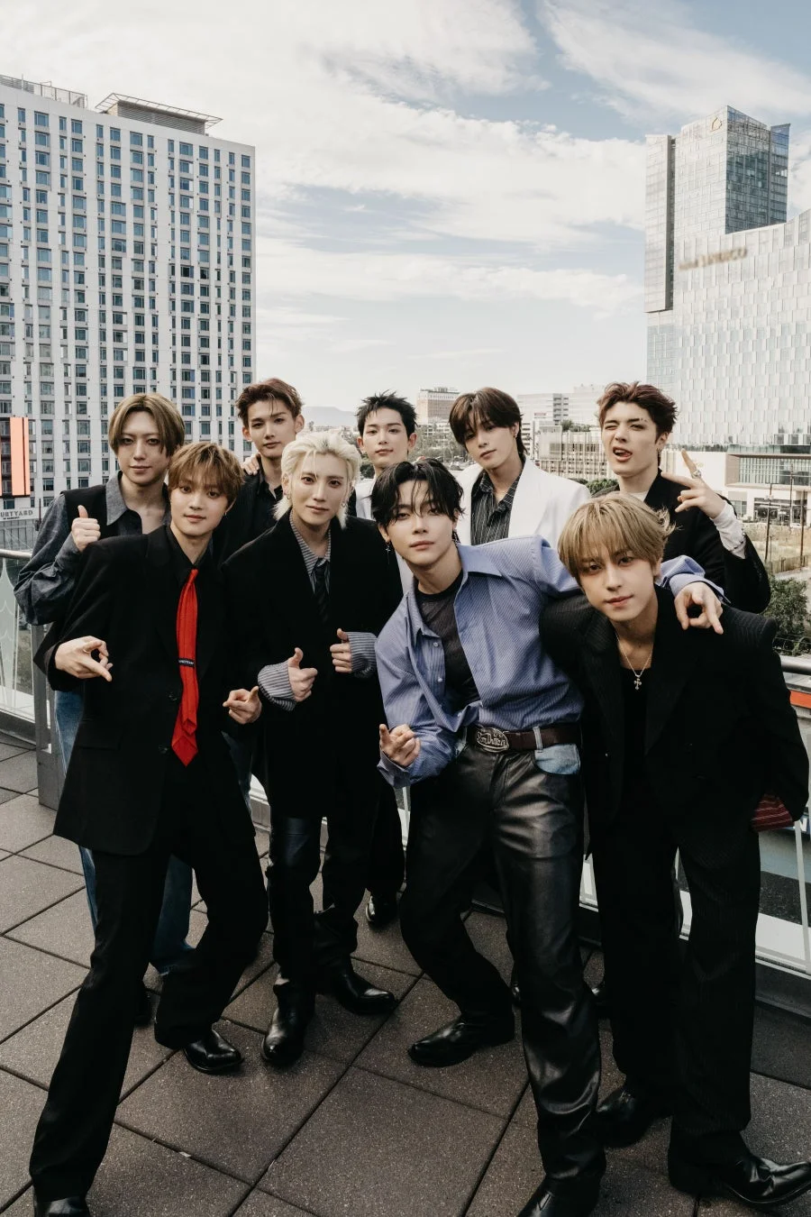 都会のビル群を背景に、屋上でポーズをとる男性アイドルグループの集合写真です。メンバーはそれぞれ個性的なファッションに身を包み、活気ある雰囲気を醸し出しています。