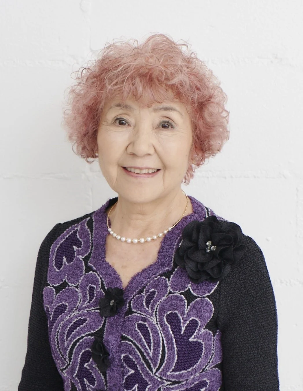 ピンク色のカーリーヘアの高齢女性が笑顔でカメラを見つめている