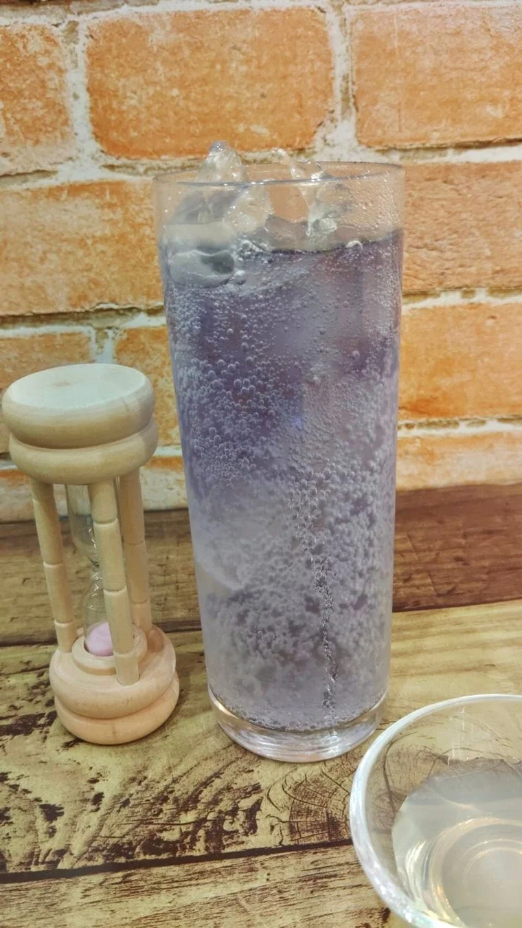 グラスに入った紫色の炭酸飲料と氷、そして小さな木製の砂時計