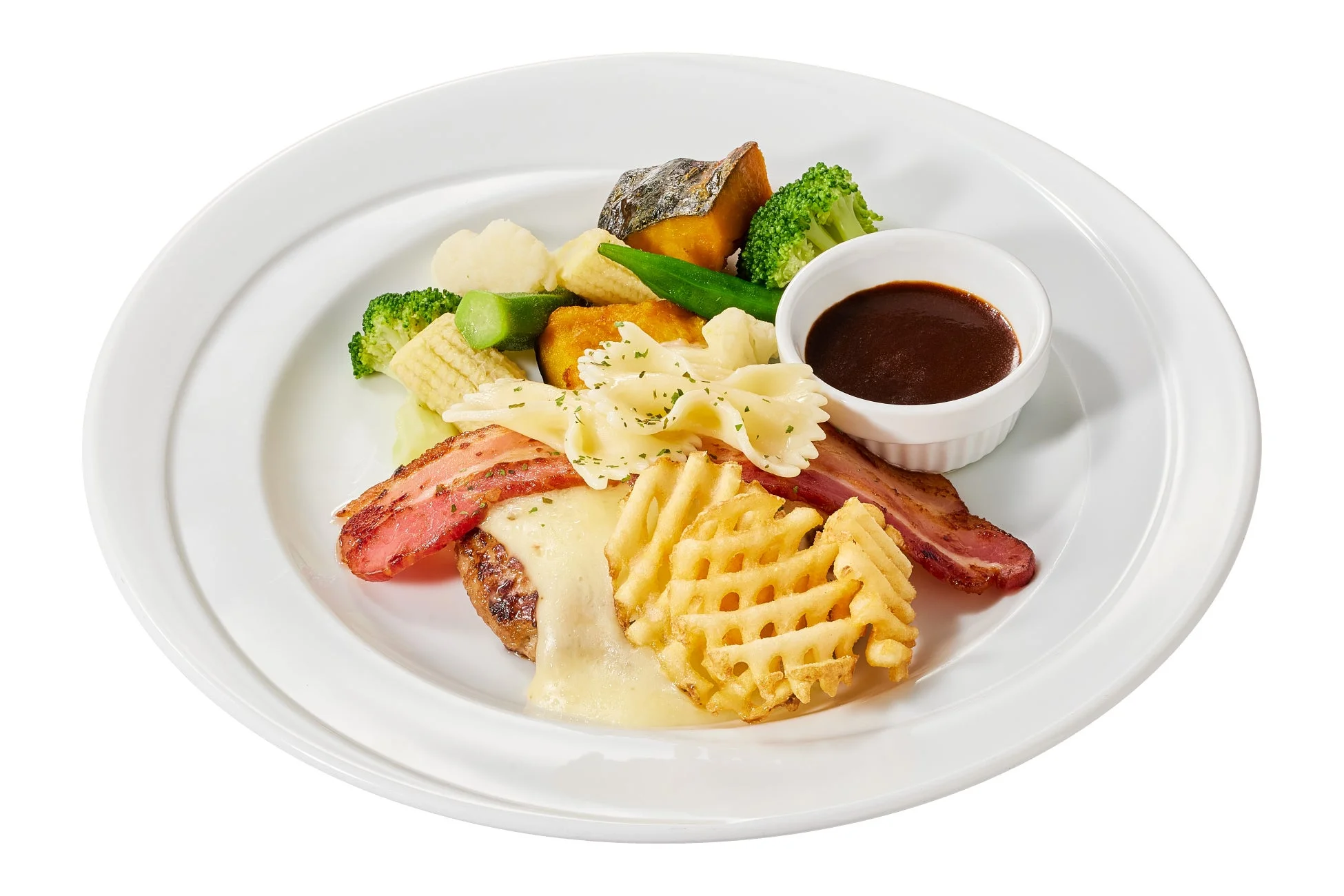 白い皿に盛られた洋食のワンプレート。チーズハンバーグ、ベーコン、ワッフルポテト、パスタ、そして彩り豊かな温野菜が添えられ、別添えのソースが食欲をそそる一品です。