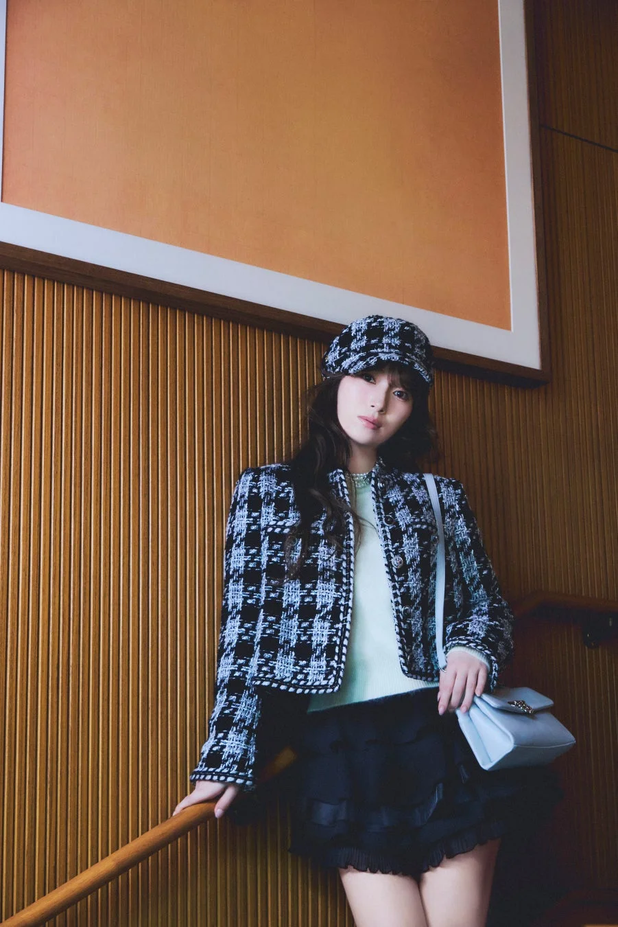 千鳥格子のジャケットとキャップを着用し、ライトブルーのハンドバッグを持った女性