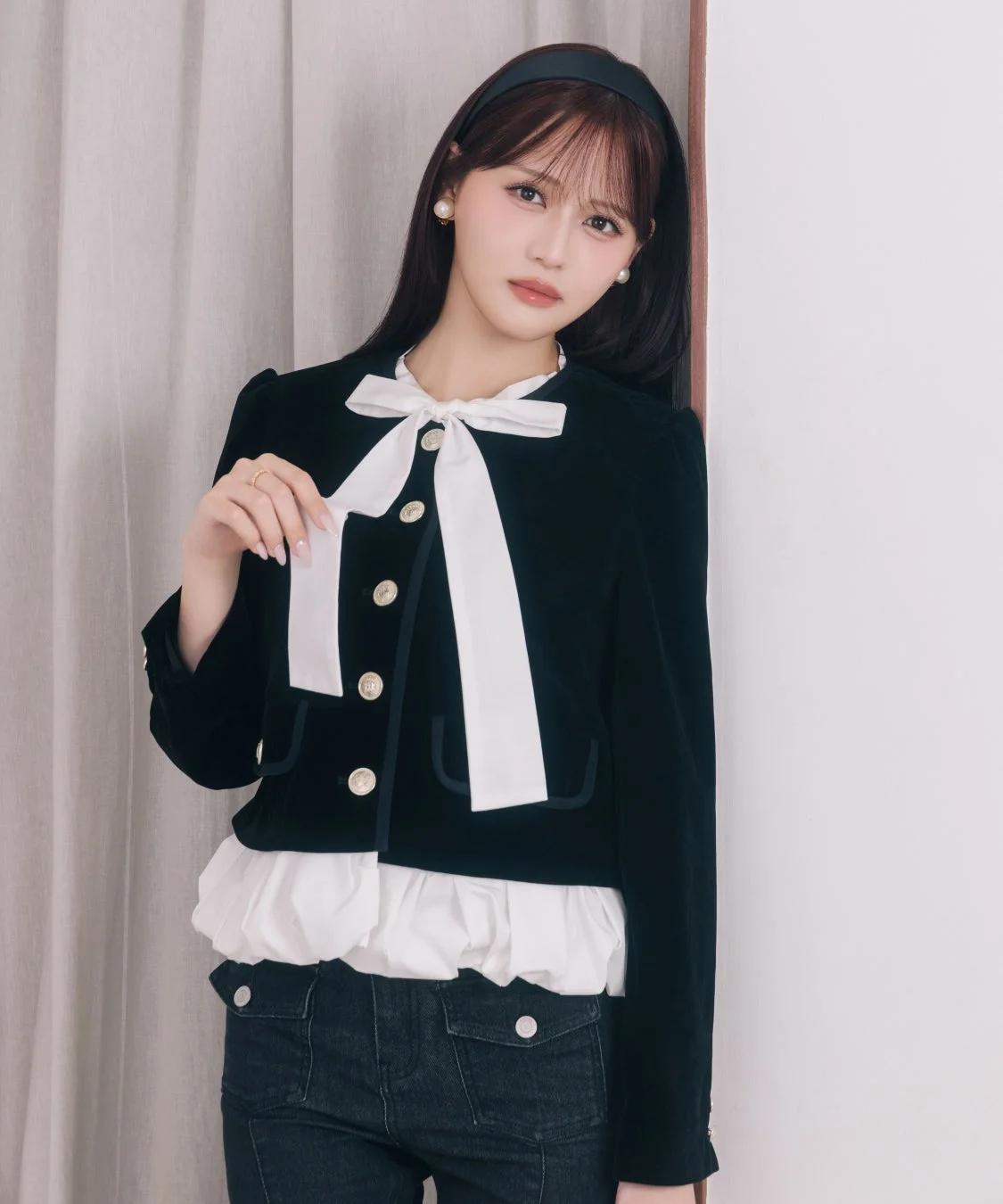 黒いショート丈ジャケットに白い大きなリボンとフリルブラウスを合わせた女性が写っています。カチューシャとパールのイヤリングを身につけ、カメラを見つめる姿が印象的です。
